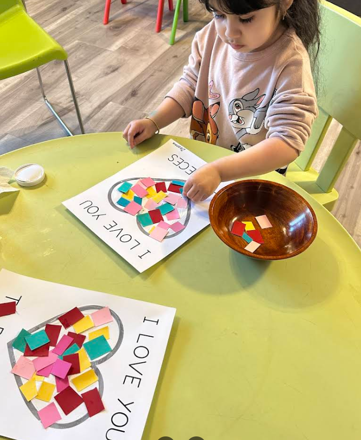 Child creating an 'I Love You' heart mosaic with colorful paper squares